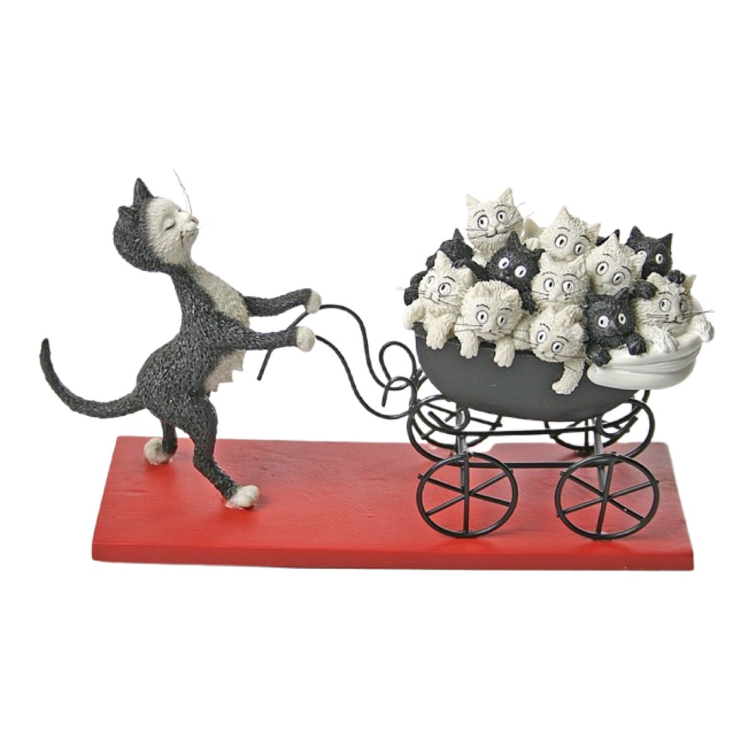 A whimsical figurine of a black-and-white cat pushing a black baby carriage filled with small black-and-white kittens, mounted on a red rectangular base against a plain white background.