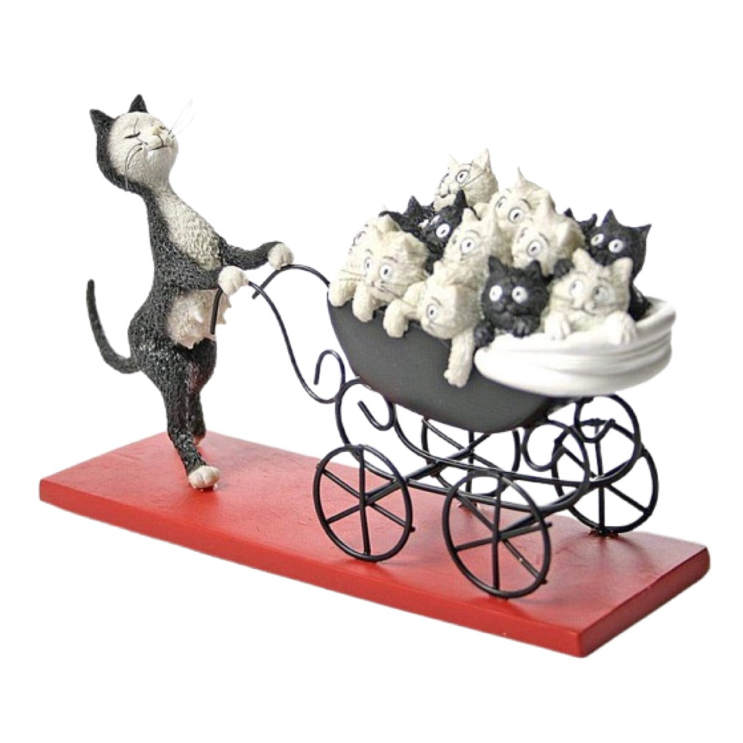 A whimsical figurine of a black-and-white cat pushing a black metal baby stroller filled with small white and black kittens, mounted on a rectangular red base against a plain white background.