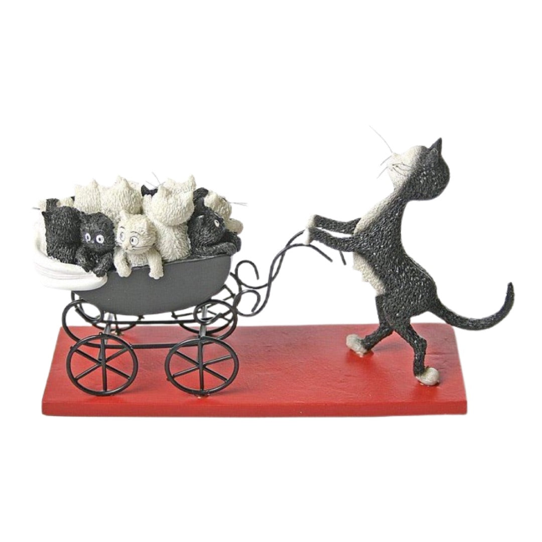 A whimsical figurine of a black cat pulling a red carriage loaded with small black and white stuffed animals, set against a plain white background.